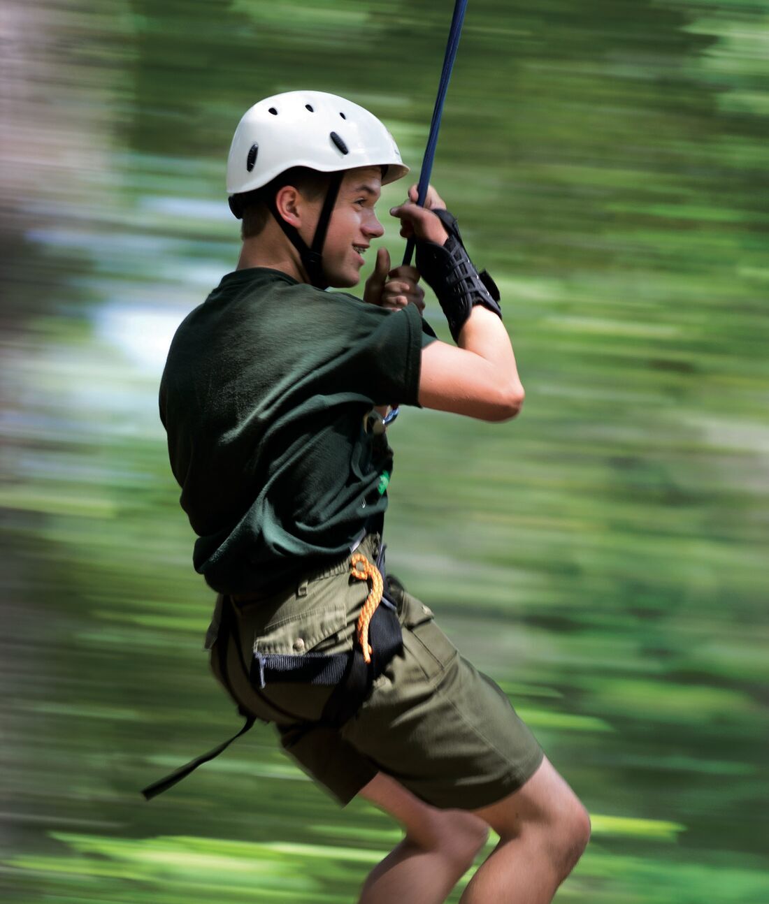 A Scout in a climbing helmet and harness rides a zip line through the trees